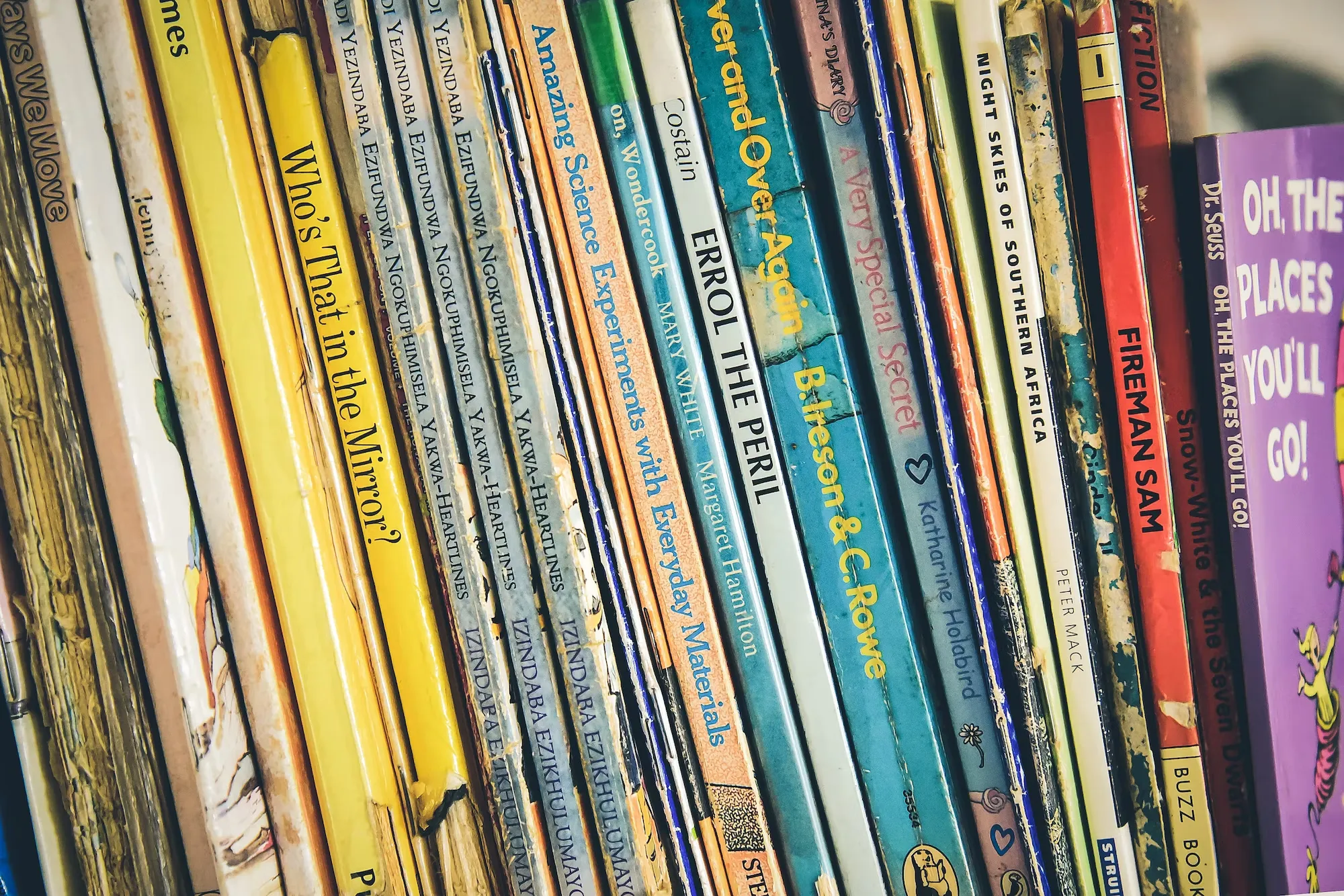 

The image shows a young girl sitting on a couch, surrounded by a variety of books of different genres. She is smiling and looks excited to explore the different stories the books have to offer. The image conveys the idea of introducing children to